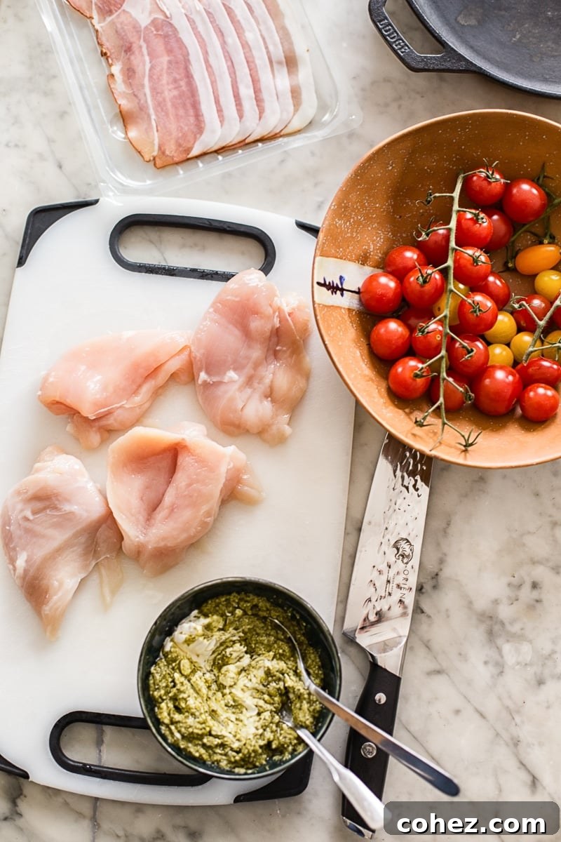 Ingredients for the recipe on a table, including pesto, tomatoes, chicken and proscuitto