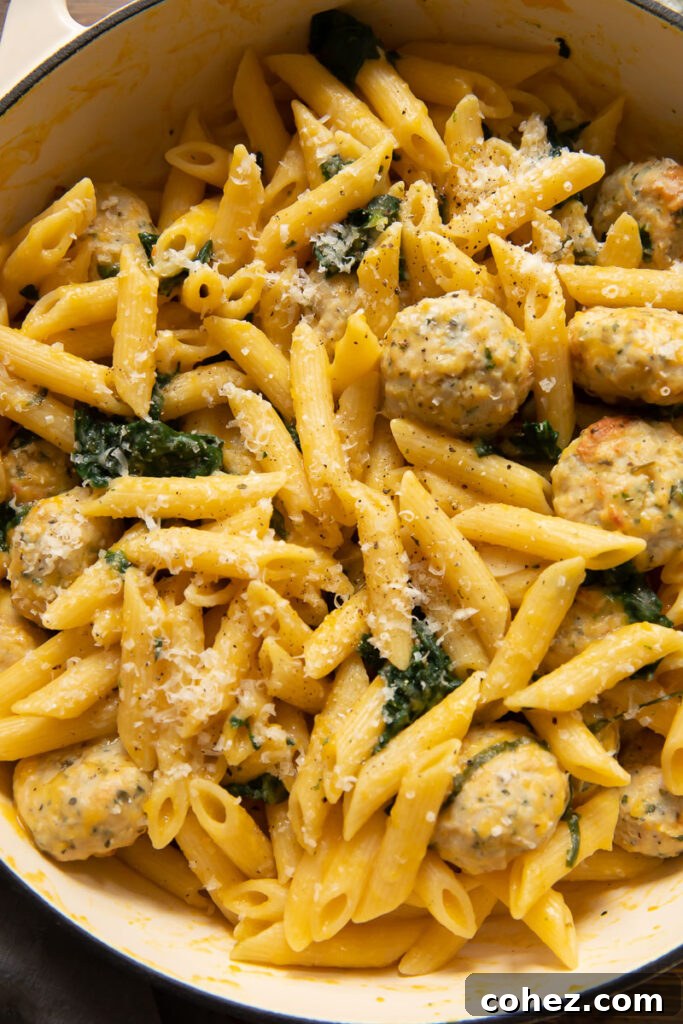 Top down view of penne pasta with juicy sausage meatballs in a vibrant pumpkin sauce, garnished with herbs