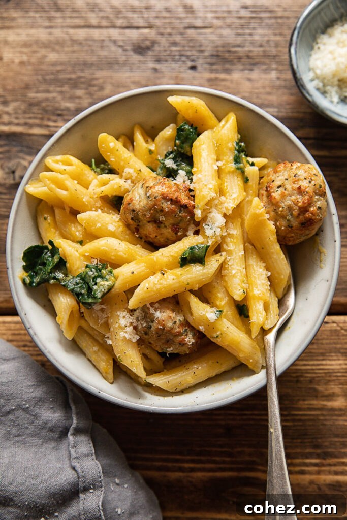 Top down view of a serving of penne pasta with sausage meatballs, pumpkin sauce, and fresh greens