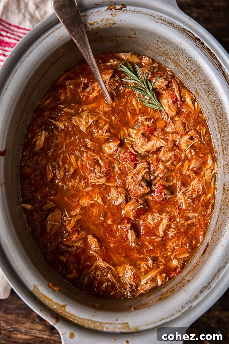 Top down of a slow cooker with the chicken ragu and a piece of rosemary