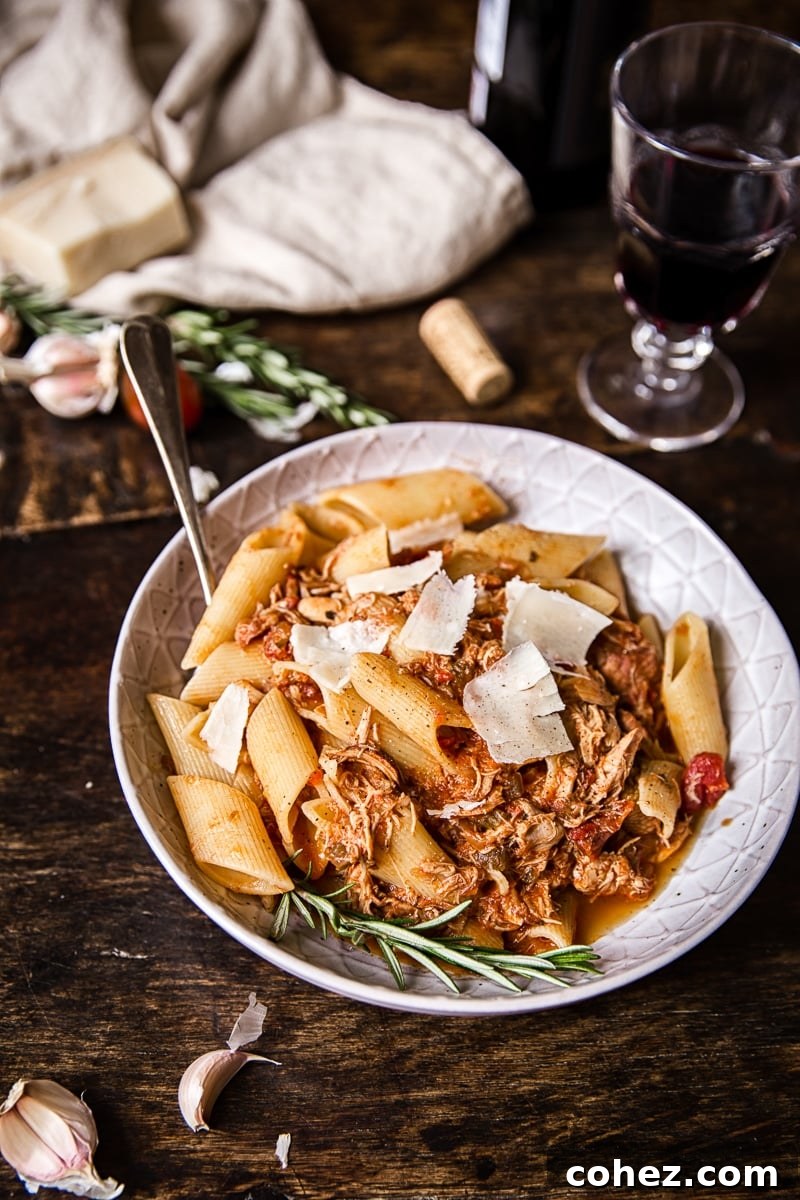 Bowl of chicken ragu pasta on a wooden table with a glass of wine