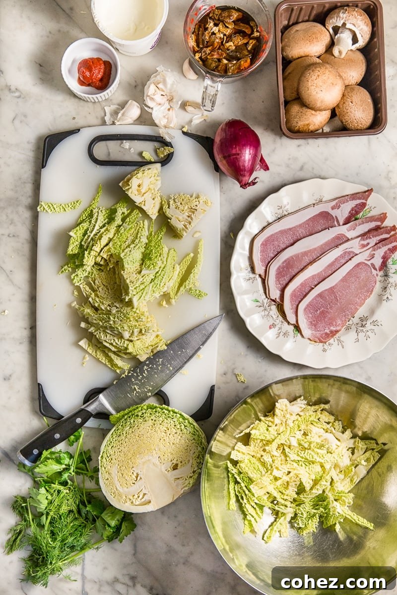 An overhead shot showcasing the fresh ingredients laid out on a table, including crisp savoy cabbage, sliced bacon, various mushrooms, and aromatic herbs, ready for preparation.