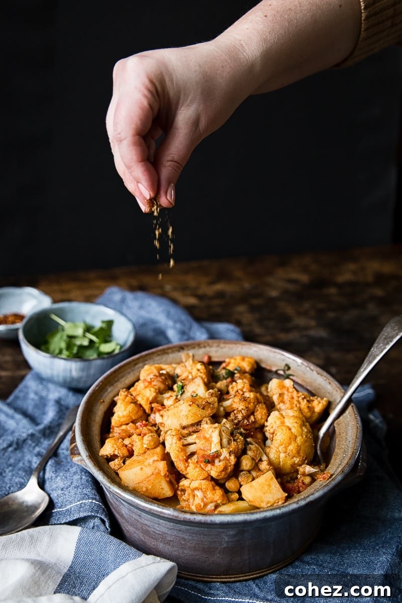 Simple Aloo Gobi Cauliflower Potato Curry 5 hand dropping spice onto cauliflower and potato curry