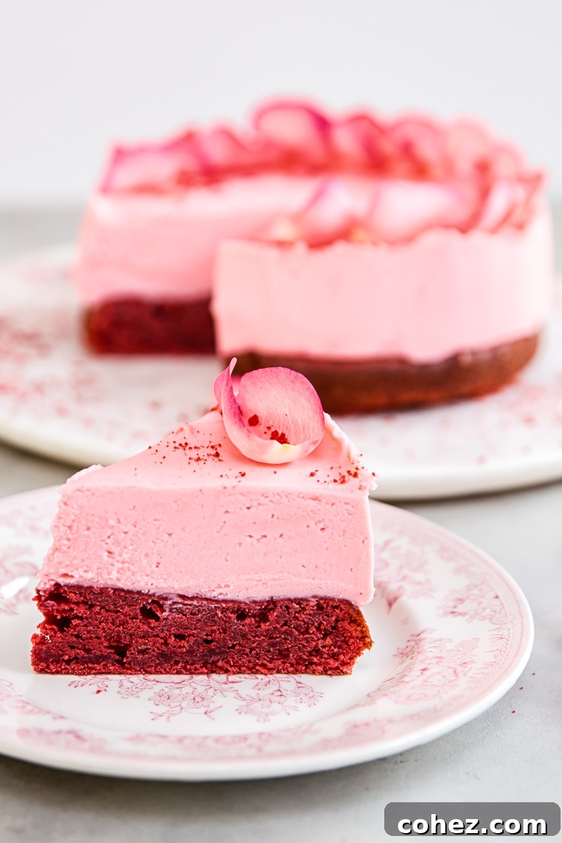 A perfectly sliced piece of red velvet cake, revealing the vibrant red sponge topped with a smooth pink white chocolate truffle layer.