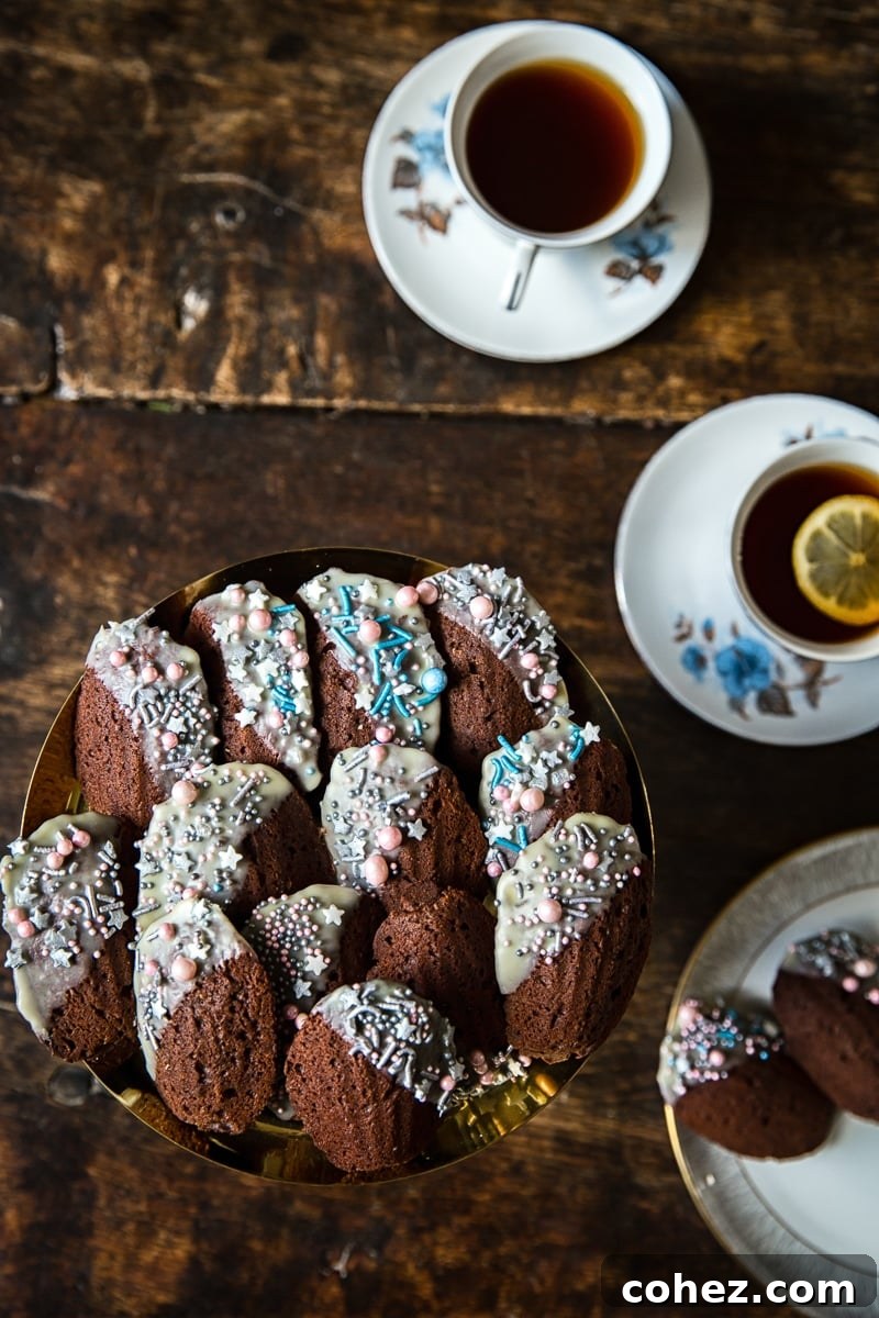 Decadent Chocolate Madeleines 2 Top down of a plate of Chocolate Madeleines with cups of tea, showcasing their perfect golden-brown exterior and iconic shell shape.