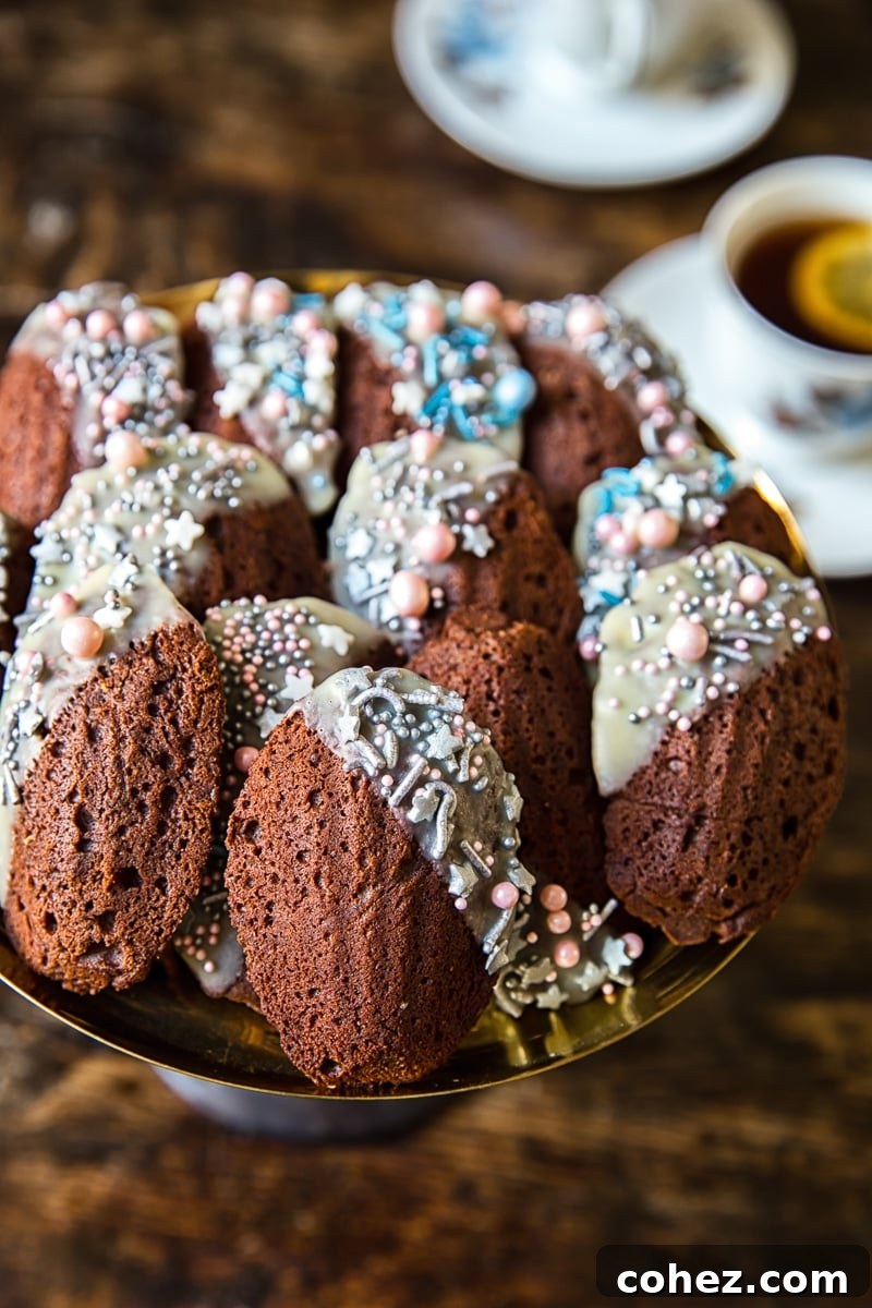 Decadent Chocolate Madeleines 3 Close-up of a plate brimming with freshly baked Chocolate Madeleines, some dipped in white chocolate and adorned with colorful sprinkles.