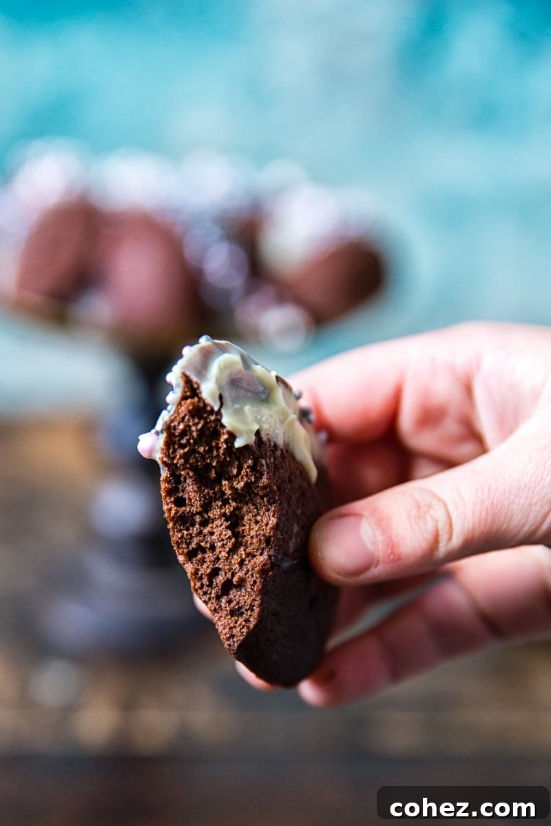 Decadent Chocolate Madeleines 5 A hand holds a Chocolate Madeleine, delicately dipped in white chocolate and sprinkled, with a tempting bite taken out, revealing its soft, rich interior.