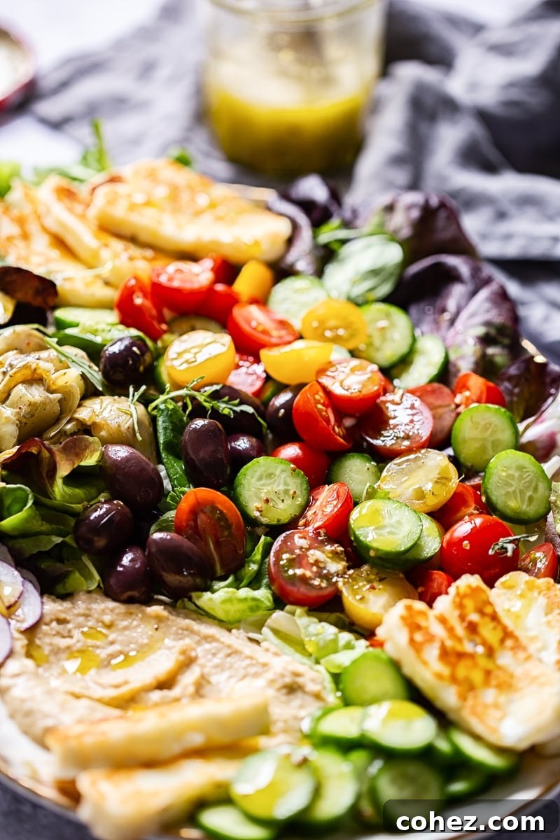 Close up of a vibrant Mediterranean salad, focusing on the fresh cherry tomatoes, crisp green leaves, and perfectly sliced cucumbers, all glistening with a light dressing.