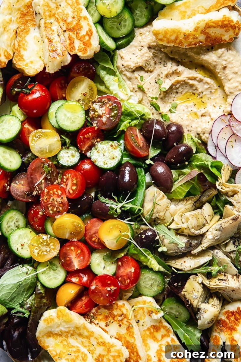 A close-up shot focusing on the vibrant red and yellow cherry tomatoes, glistening with dressing, nestled among fresh greens in the Mediterranean salad.