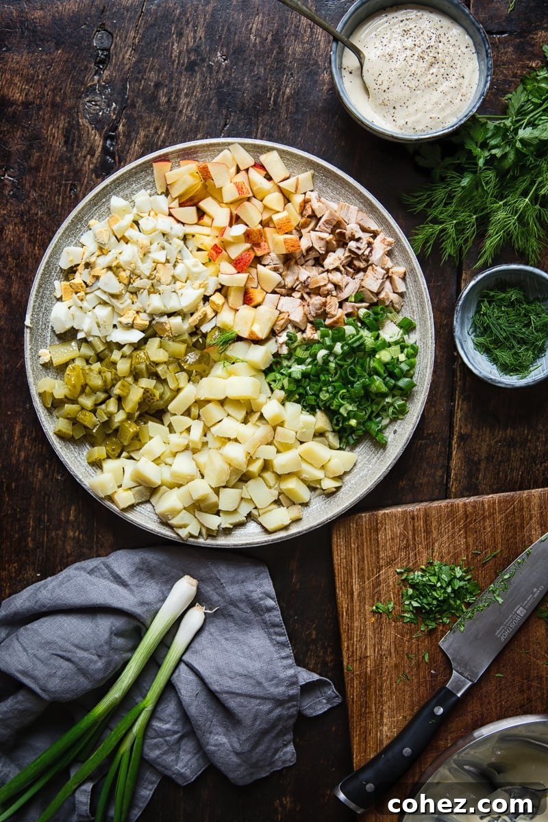 A vibrant display of fresh Russian salad ingredients on a platter, including green onions, herbs like dill and parsley, a cutting board, and a bowl of creamy salad dressing.