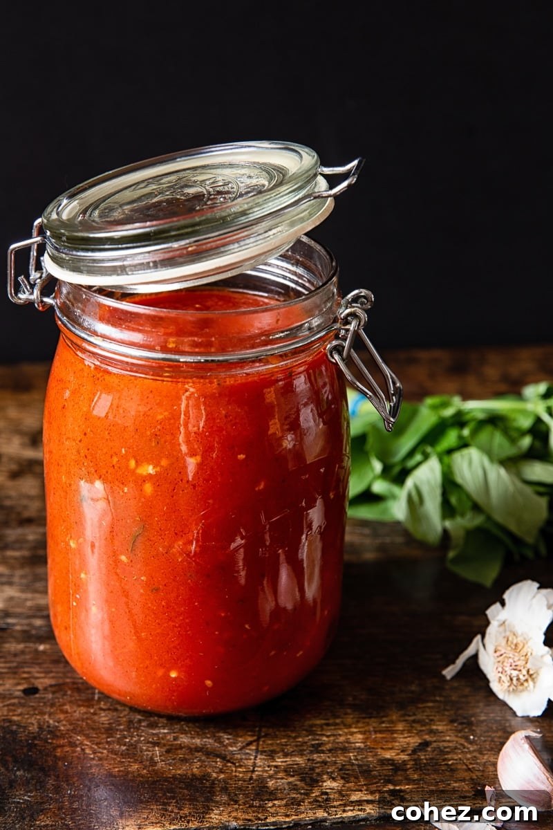 Jar of vibrant red homemade spaghetti sauce next to fresh garlic and basil on a rustic wooden table