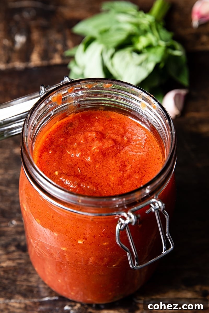 An open jar filled with fresh homemade spaghetti sauce, garnished with basil, set against a blurred background