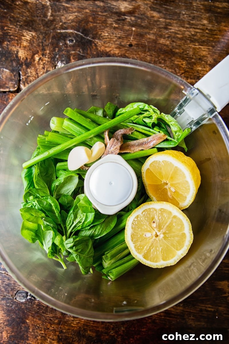 Fresh green herbs and lemon in a food processor, ready for blending Green Goddess dressing