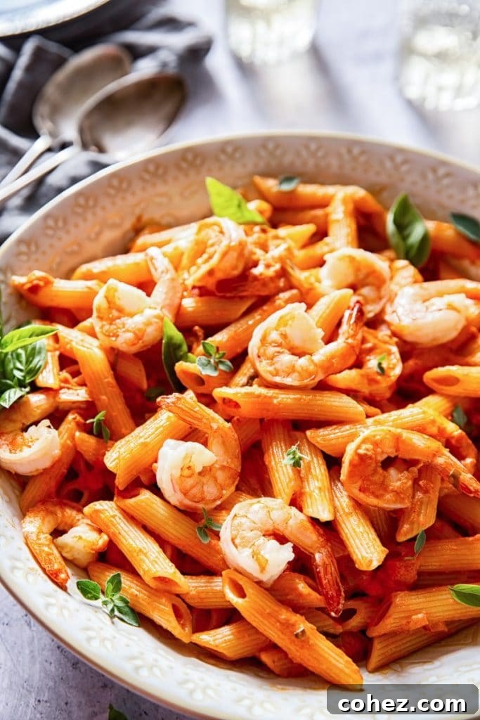 Side view of a serving bowl of penne alla vodka with shrimp, garnished with fresh herbs