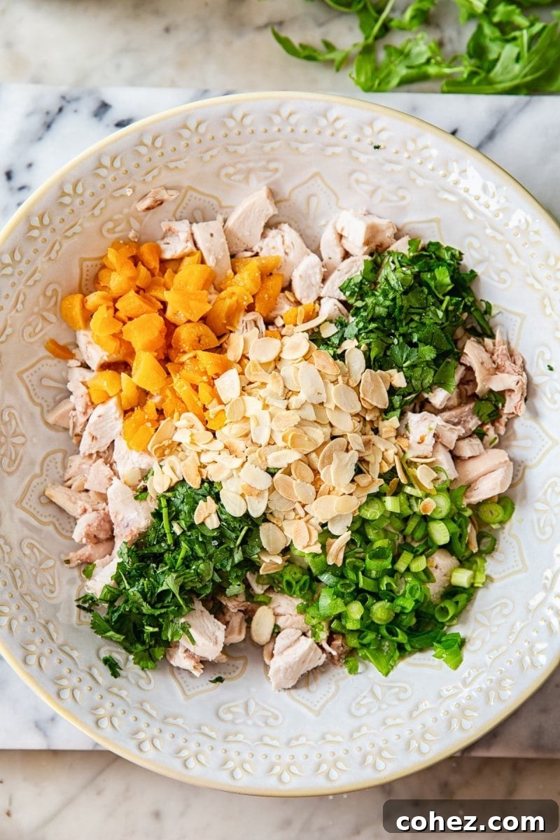 A wide bowl filled with the fresh ingredients for Coronation Chicken Salad before they are mixed with the dressing.