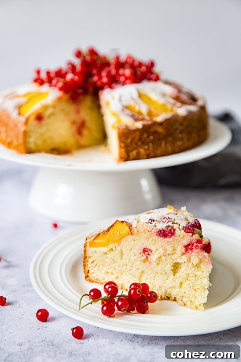 Golden Peach and Red Berry Summer Cake 4 A slice of the peach and red berry cake in the foreground, with the whole cake behind
