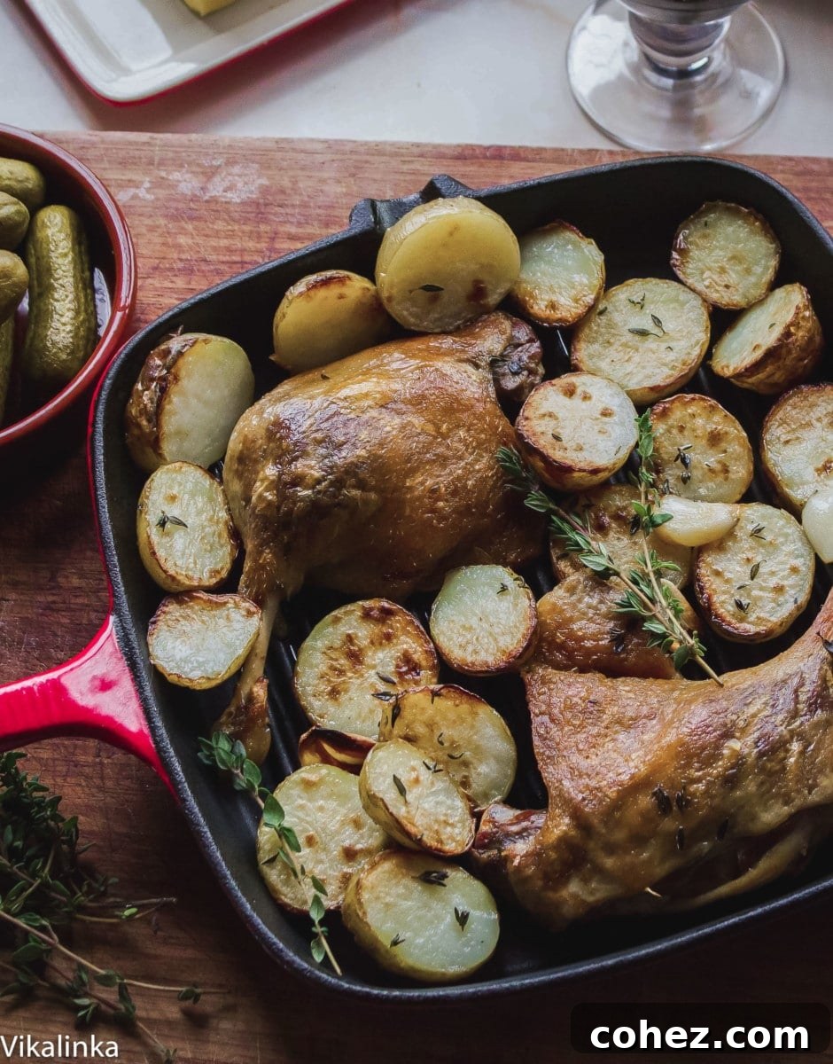Top down view of a pan filled with cooked duck confit and perfectly roasted potatoes, garnished with fresh herbs, ready to serve