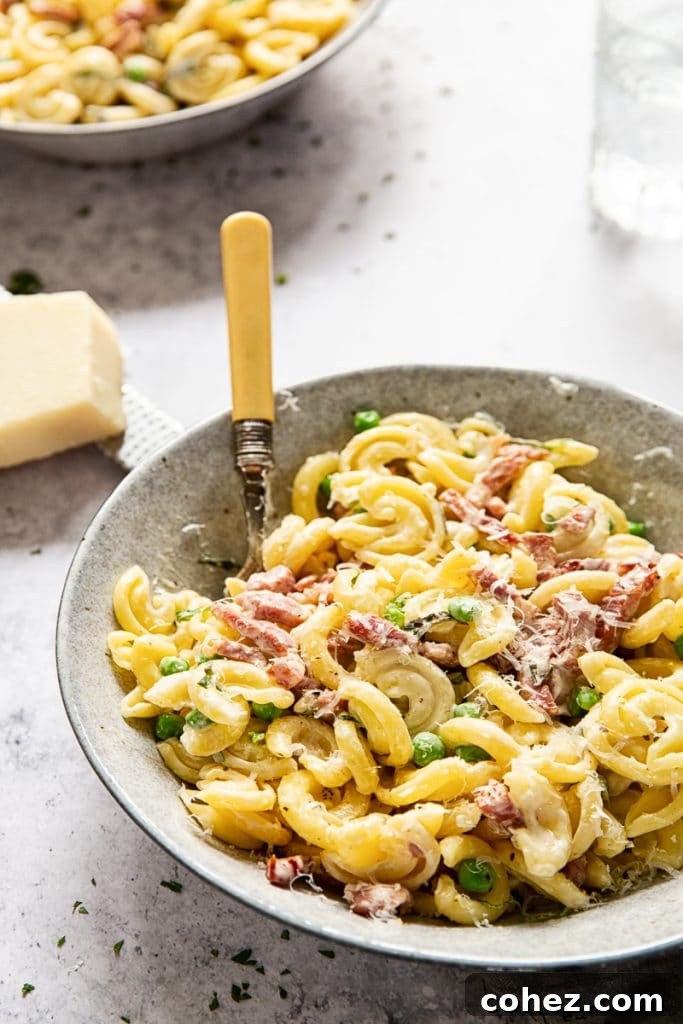 Bowl of Creamy Pasta with Peas and Pancetta with a fork inserted, ready to be enjoyed.