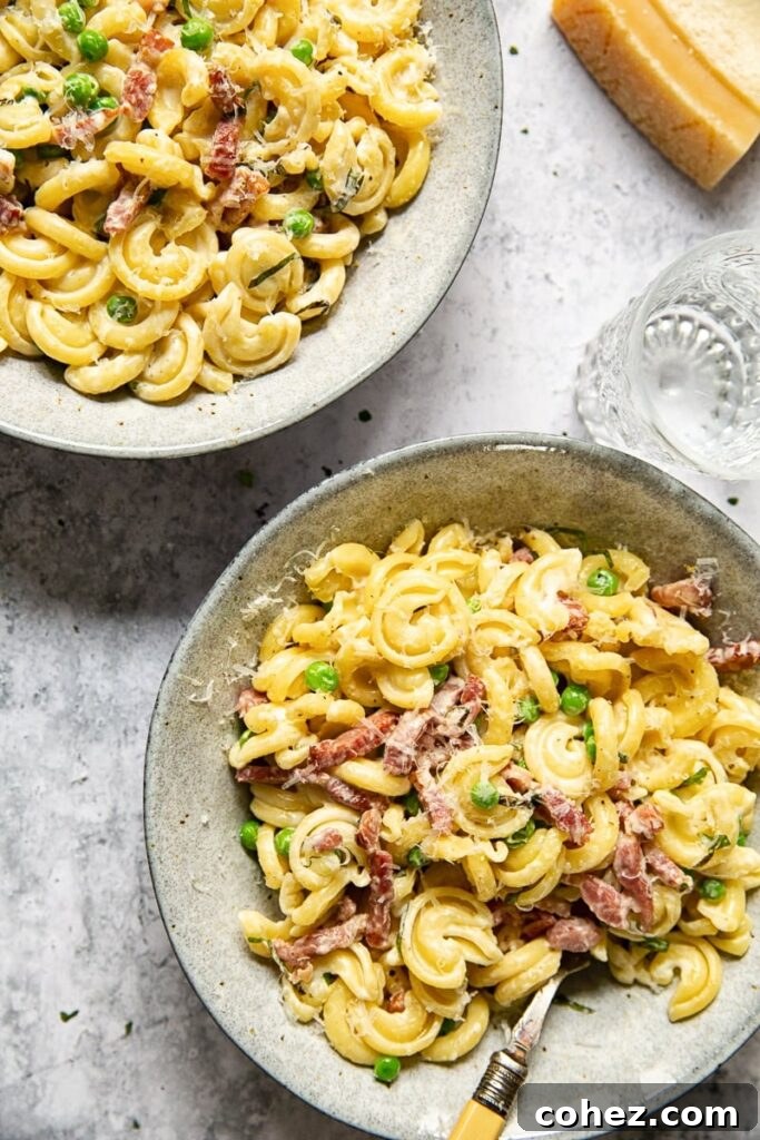 Top-down view of two inviting bowls of creamy pasta with peas and pancetta, alongside a refreshing water glass.
