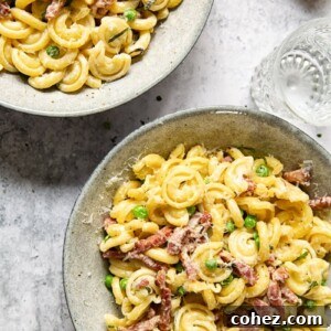 top down view of two bowls of pasta with pancetta and peas with water glass