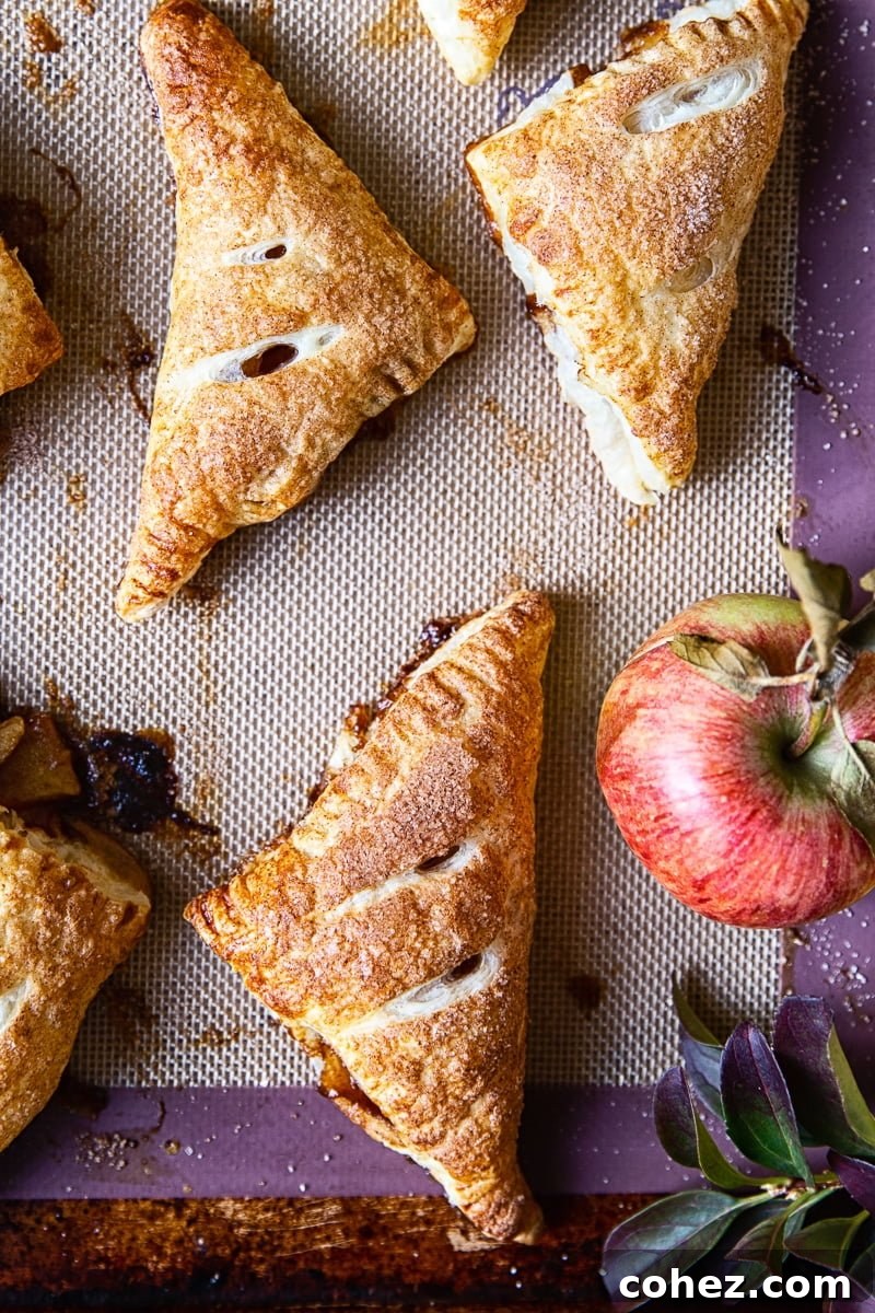 Freshly baked apple turnovers next to a vibrant apple, ready to be enjoyed.