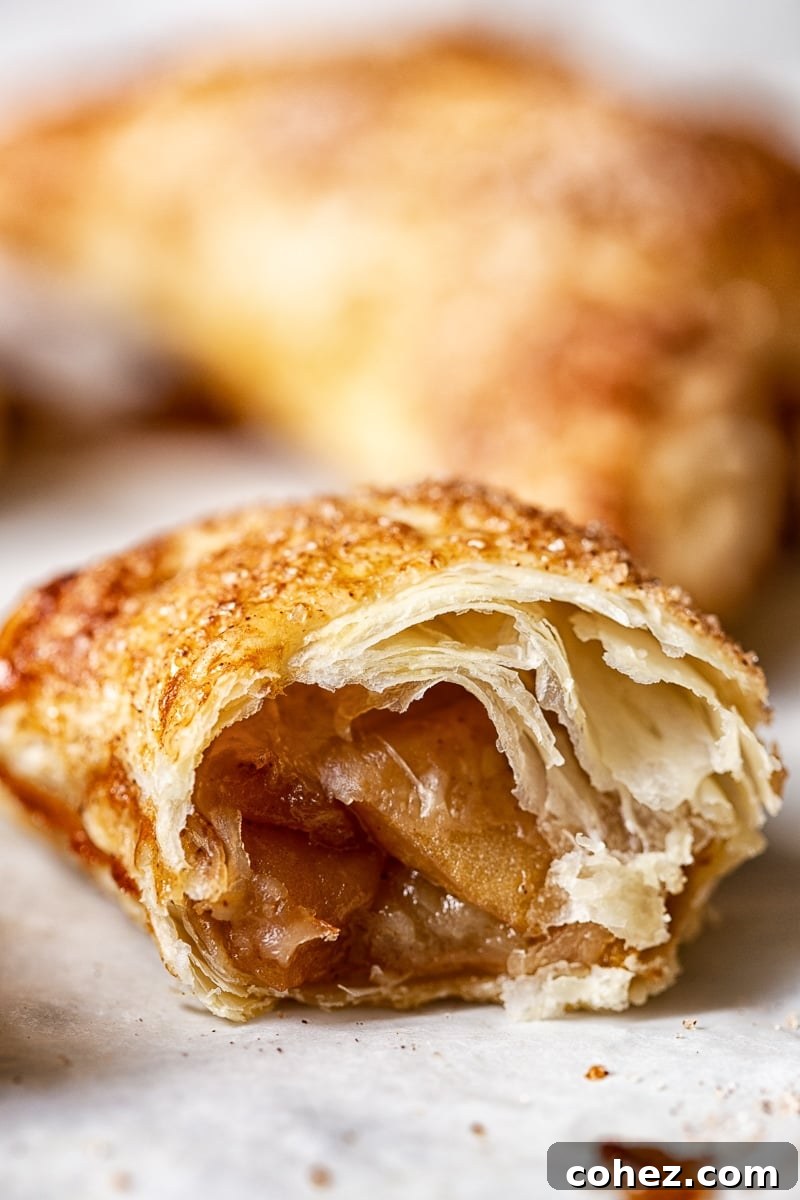 A close-up shot of an apple turnover with a bite taken out, revealing the soft, spiced apple filling and flaky crust.