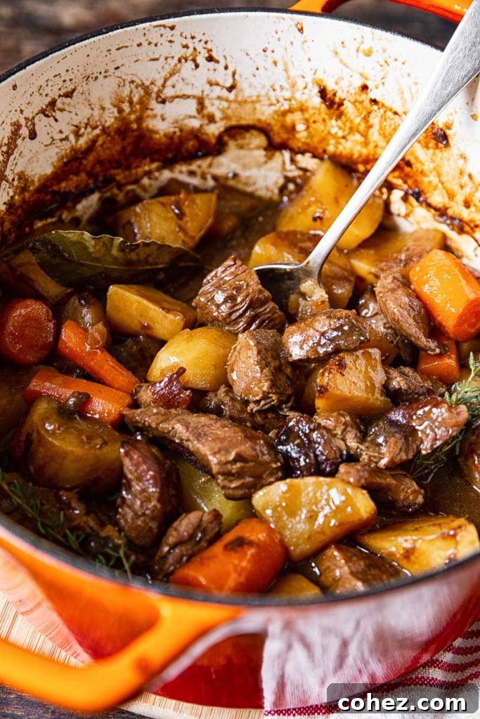 Irish Beef Stew simmering in a vibrant orange Dutch oven, promising warmth and flavor.