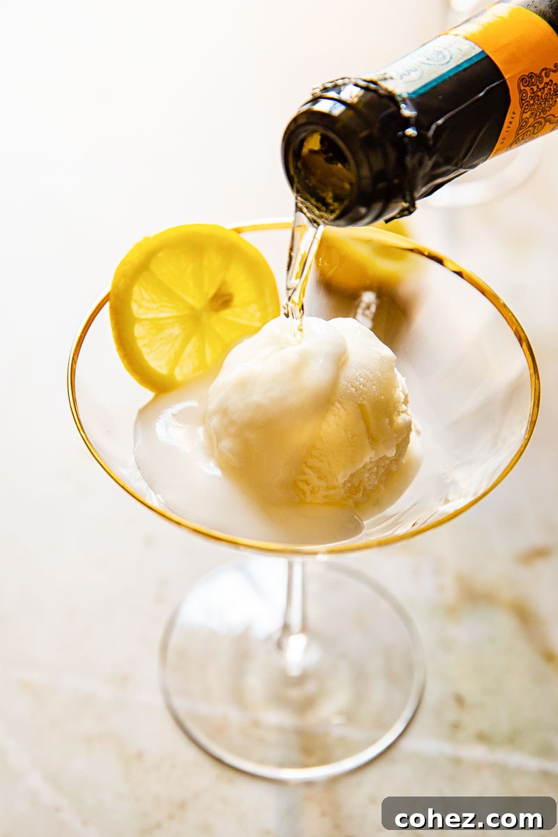 A bottle neck pouring sparkling Prosecco into a cocktail glass filled with lemon sorbet and a lemon slice.