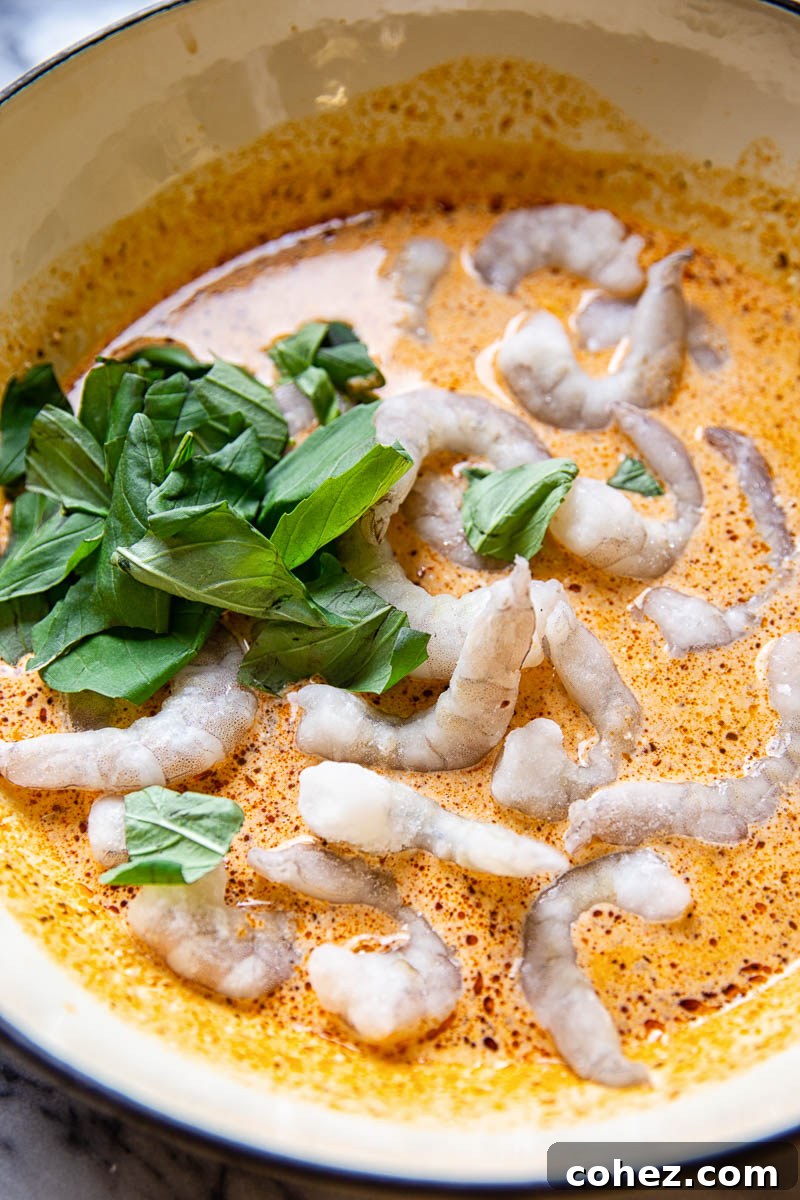 Fresh prawns simmering in a creamy sun-dried tomato sauce with basil in a white pan.