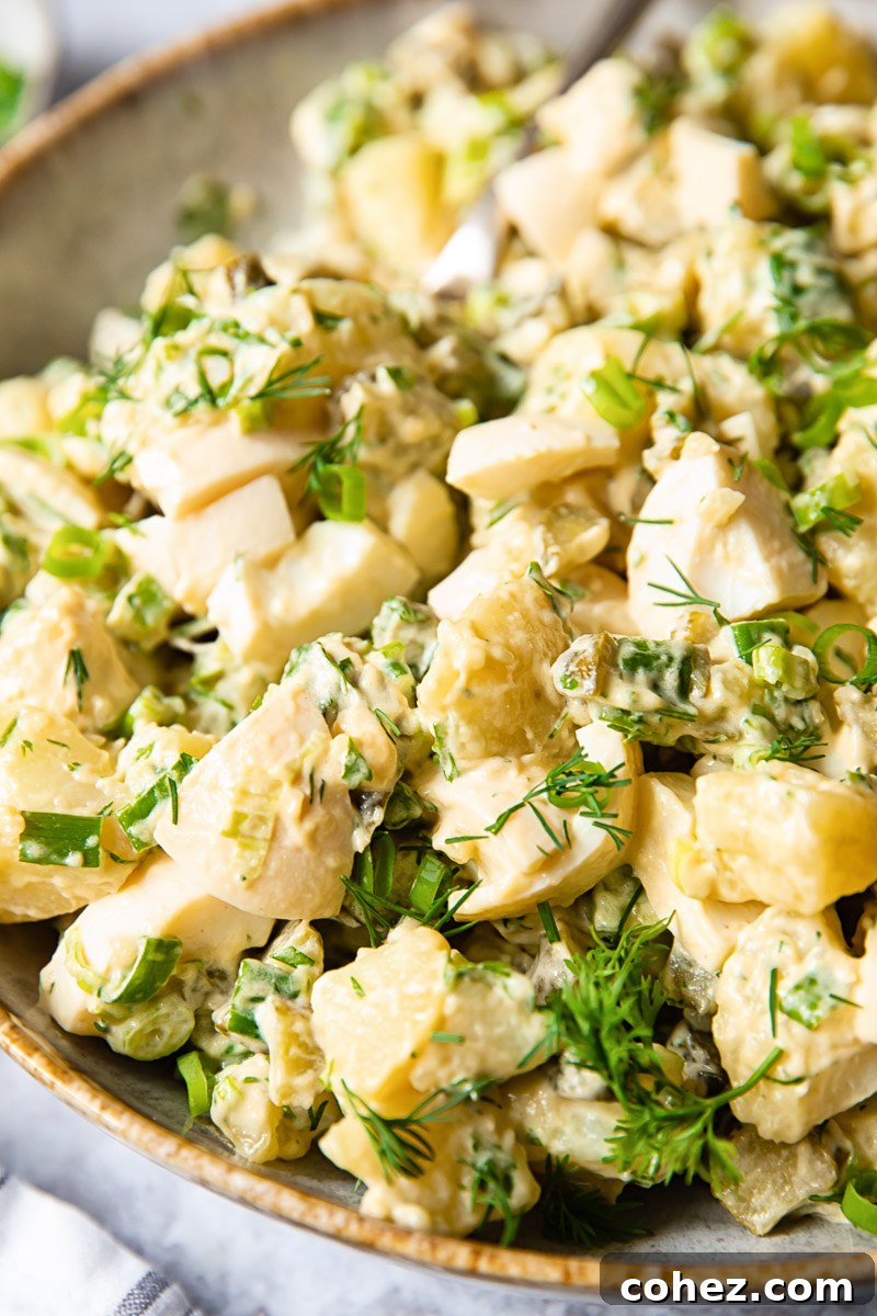 Side view of a serving of dill potato salad, highlighting its creamy texture and fresh garnishes.