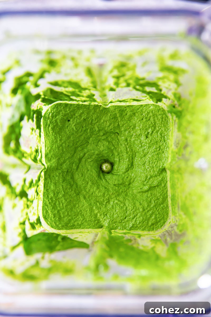 Freshly blended spinach pesto being made in a food processor or blender, showing its vibrant green color and smooth texture.