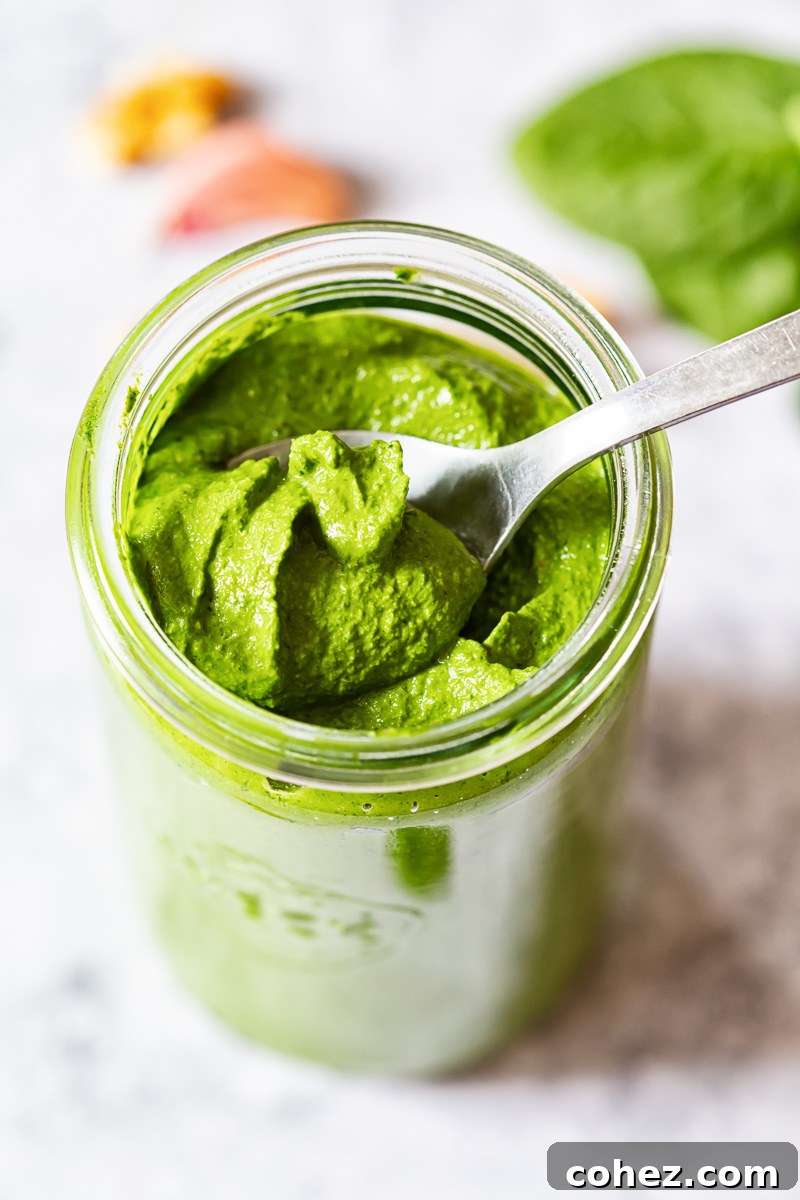 A spoon scooping up vibrant green spinach pesto from a glass jar, with a top-down view highlighting its rich texture.
