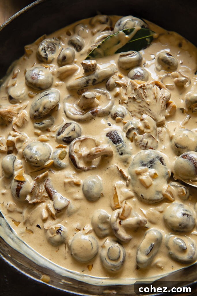 A close-up view of the rich, creamy mushroom stroganoff sauce simmering in a pan, showcasing its luxurious texture before being combined with pasta.