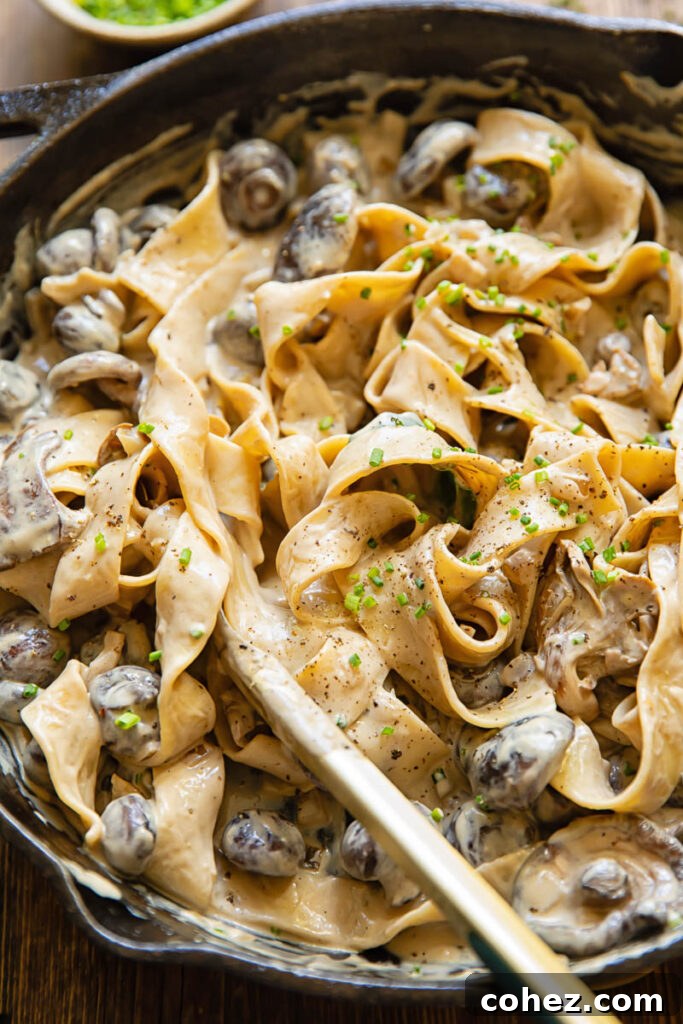 A large pan of creamy mushroom stroganoff with a set of serving tongs, ready to scoop out generous portions of the hearty dish.