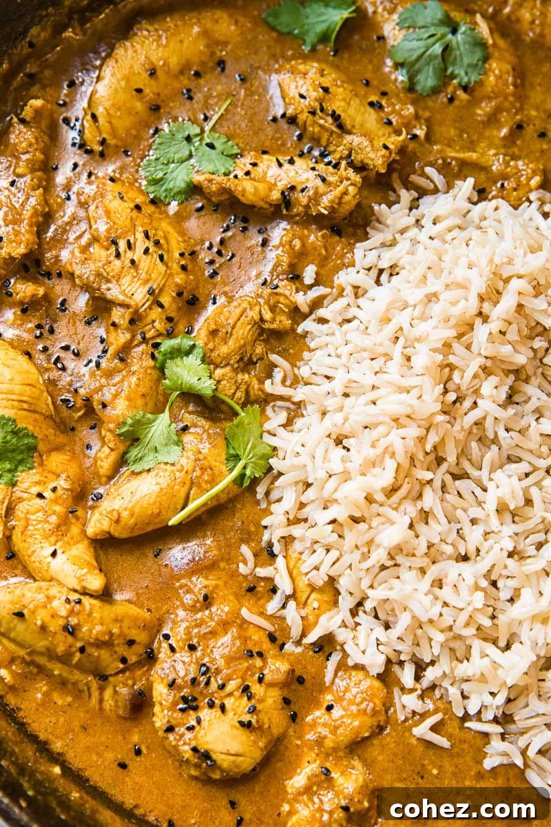 Close-up of a bowl of Chicken Korma, rich and creamy, garnished with fresh herbs, ready to be served with brown basmati rice.