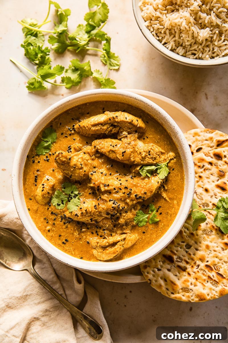 A vibrant bowl of Chicken Korma, beautifully plated with fresh cilantro, served alongside fluffy naan bread and wholesome brown basmati rice, ready to be enjoyed.
