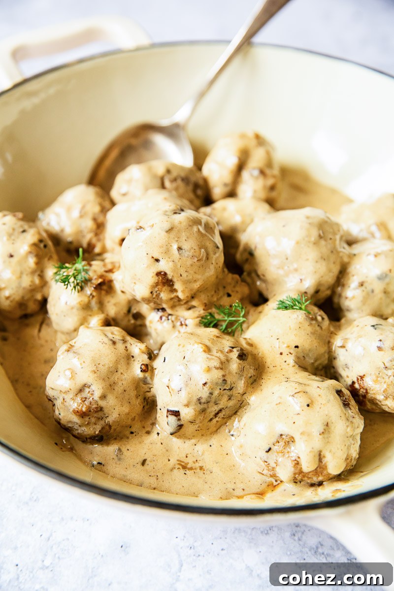 Meatballs in cream sauce shown in a white pan, garnished with fresh herbs.