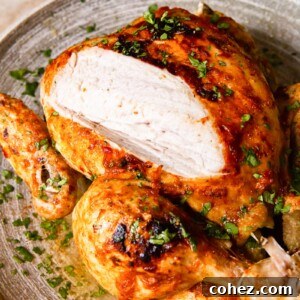 Whole Chicken on platter with a part of breast sliced off, highlighting juicy meat.