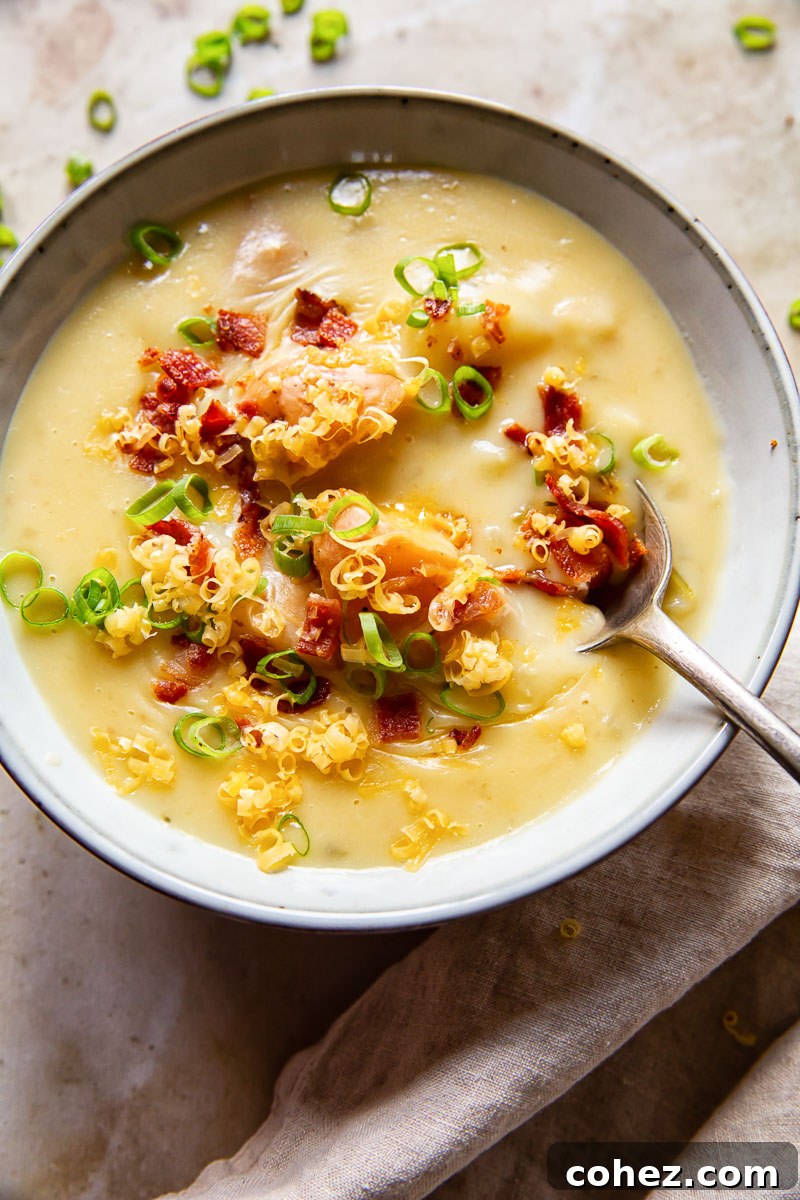 A close-up of a grey bowl filled with creamy Instant Pot potato soup, generously topped with fresh green onions, crispy bacon pieces, and grated cheese, with a spoon resting in the bowl.