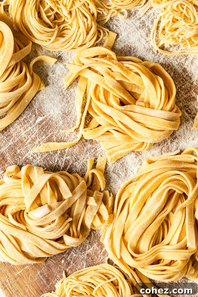 Freshly made fettuccine pasta rests on a wooden board, dusted lightly with flour, ready for cooking.