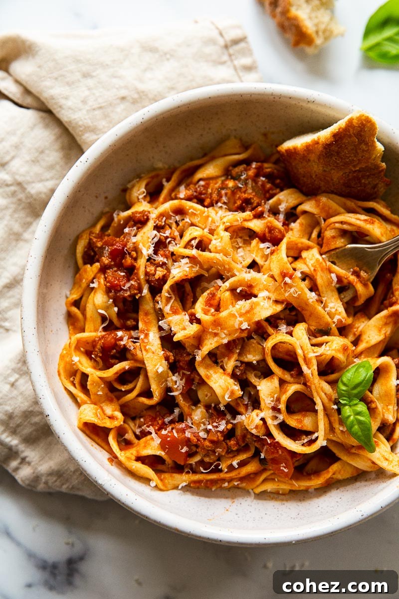 A bowl of freshly cooked tagliatelle pasta, generously topped with a rich bolognese sauce and garnished with fresh herbs.