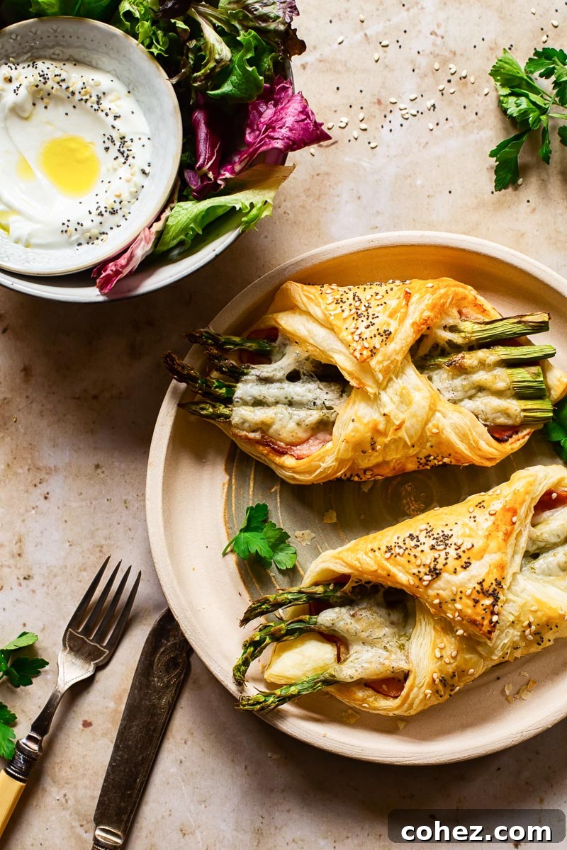 Delicious golden puff pastry appetizers with ham, cheese, and asparagus on a serving plate, ready to be enjoyed.