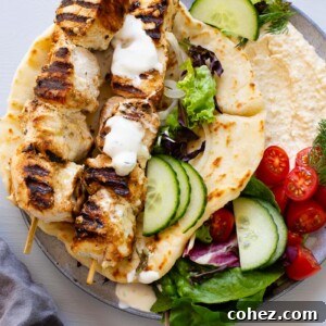chicken souvlaki skewers on top of pita bread filled with hummus and vegetables