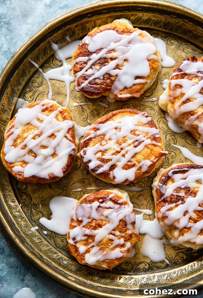 Overhead view of perfectly golden-brown apple fritters, generously drizzled with a sweet sugar glaze, arranged on an elegant platter.
