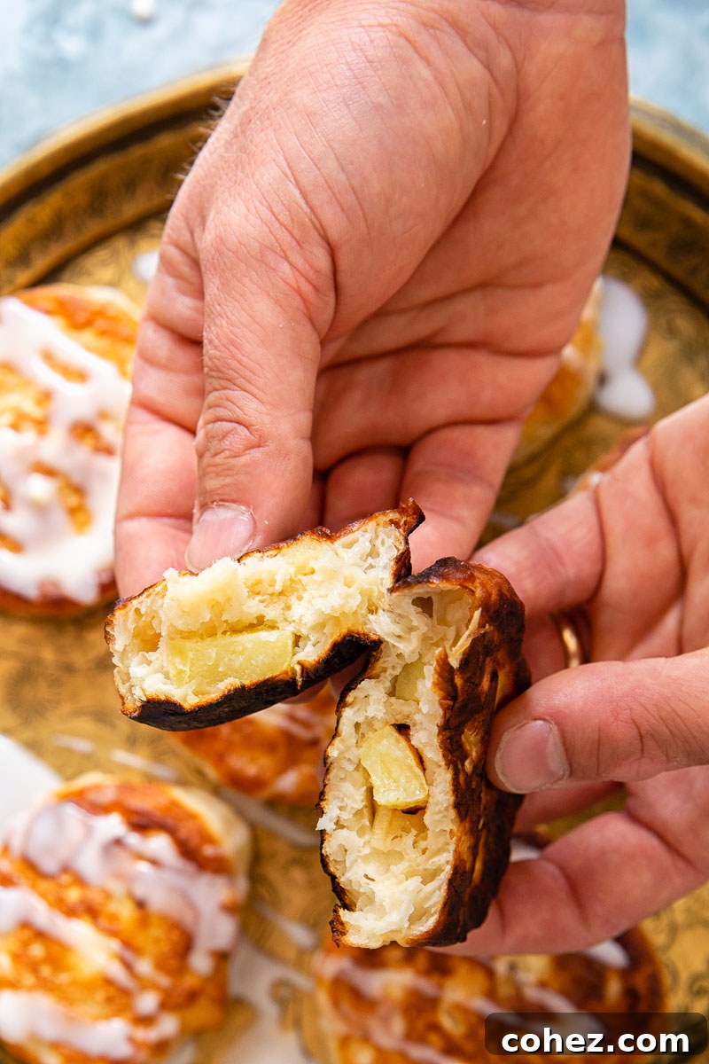 A close-up view of an apple fritter broken in half, revealing juicy apple chunks embedded within its soft, fluffy interior.