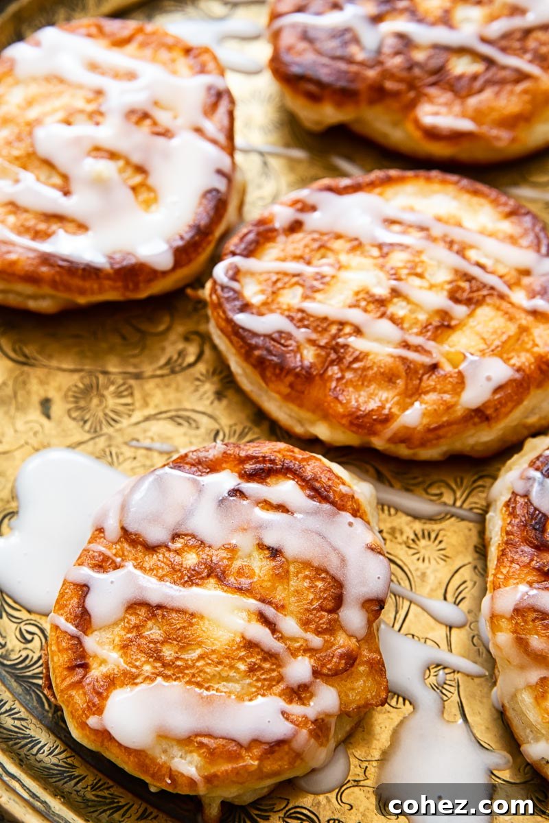 A delectable close-up of golden-brown apple fritters generously drizzled with a glistening sugar glaze, highlighting their inviting texture and sweet finish.