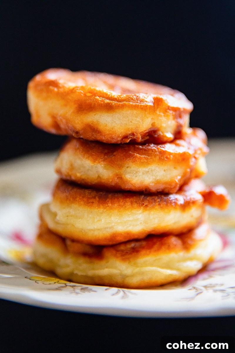 A beautifully presented stack of four golden-brown apple fritters, perfectly arranged on a plate, ready to be enjoyed.