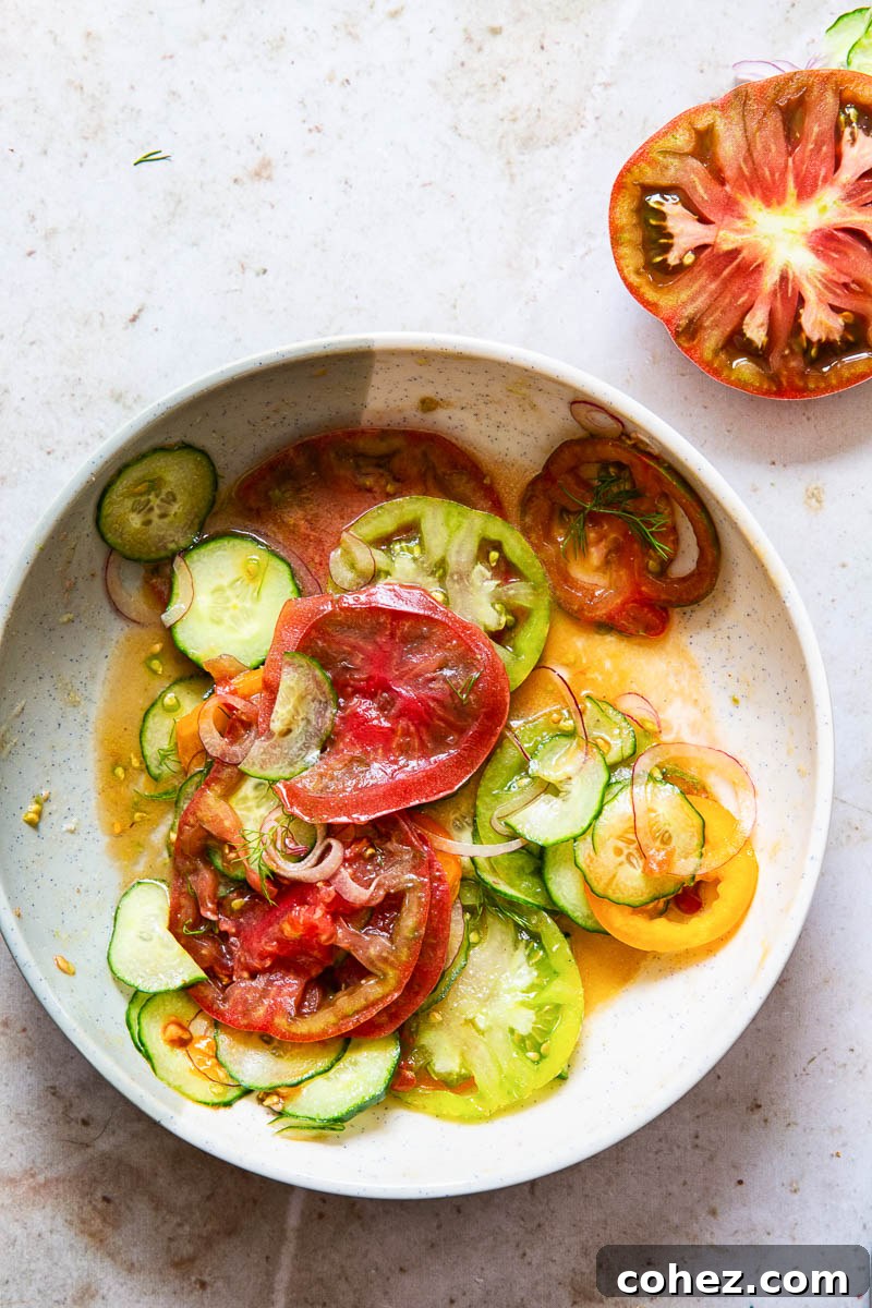 A bowl of freshly prepared heirloom tomato and cucumber salad, highlighting the thin slices of vegetables and a light dressing