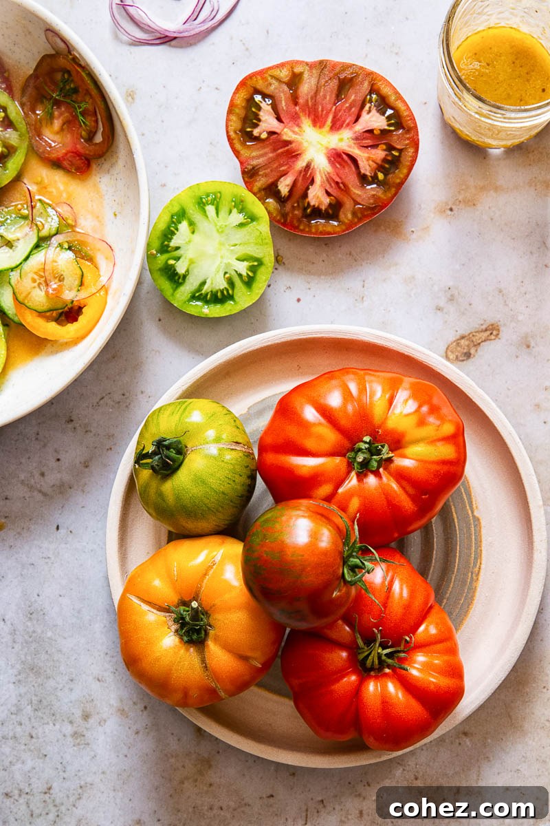Assortment of cut heirloom tomatoes on a plate next to a small bowl of salad dressing, ready for preparation