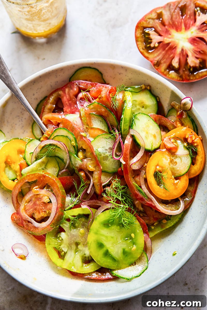 Close-up of a cucumber tomato salad being gently tossed in a bowl, showing the uniform thin slices